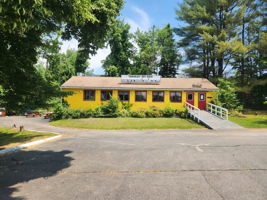 The bright yellow detached dining building, known as the "Tamarack Out-Back," offers patrons a comfortable indoor space with expansive windows and multiple tables to enjoy their meals.